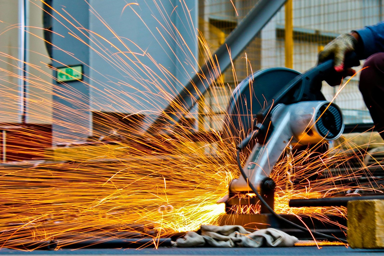 A worker operates a grinder cutting metal, creating a vibrant display of sparks in an industrial setting.